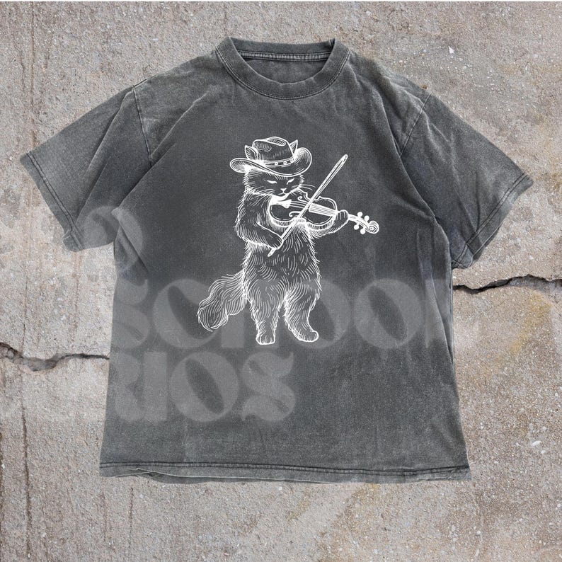 May include: A charcoal gray t-shirt featuring a white illustration of a cat wearing a cowboy hat and playing a violin. The shirt has a vintage, washed appearance. The word "SCHOOL" is faintly visible in the background.