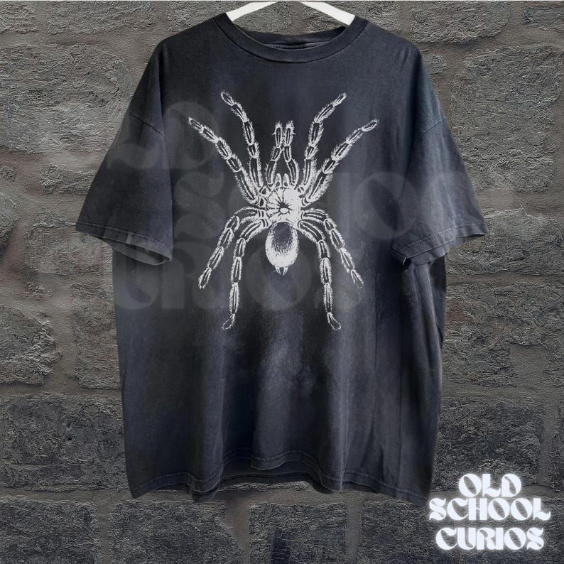 Peut inclure: T-shirt noir avec un motif d'araign&eacute;e tarentule blanche. Le t-shirt a un aspect vintage et d&eacute;lav&eacute;. Les mots "OLD SCHOOL CURIOS" sont imprim&eacute;s en blanc en bas &agrave; droite.
