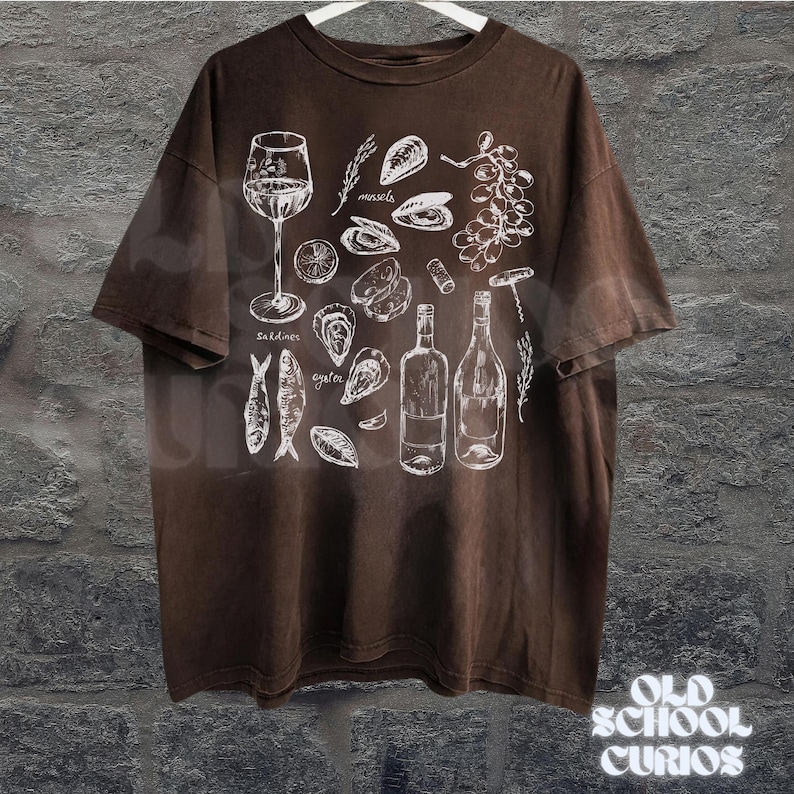 May include: Brown t-shirt with a white illustration of seafood and wine elements, including sardines, oysters, mussels, wine bottles, and a wine glass. The shirt has the text "Old School Curios" at the bottom.