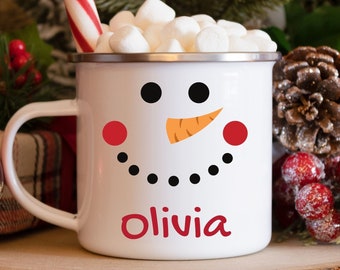 Peut inclure: Mug en émail blanc avec un visage de bonhomme de neige et le nom Olivia imprimé au bas. Le mug est rempli de guimauves et d'une canne en sucre rouge et blanche.