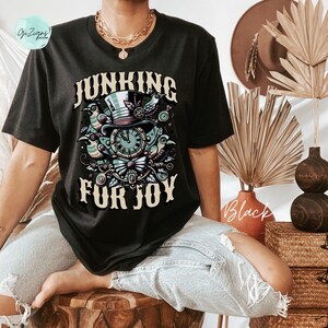 May include: Black t-shirt with a graphic of a clock, birds, and a top hat. The text "Junking for Joy" is printed on the shirt.