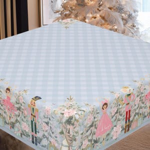 Peut inclure: Une nappe à carreaux bleu clair et blanc avec une bordure décorative représentant des illustrations de ballerines, de casse-noisettes et de feuillage d'hiver. La nappe est conçue pour une ambiance festive.