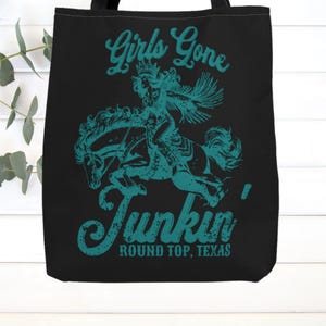 May include: Black tote bag with a teal graphic of a woman riding a horse. The graphic says "Girls Gone Junkin' Round Top, Texas".