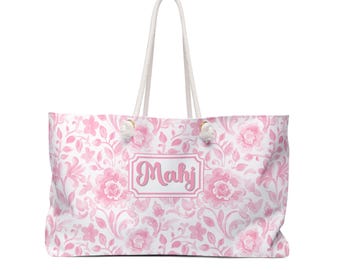 May include: A large tote bag with a floral pattern in shades of pink and white. The bag features a white rope handle and the name "Mahj" in a pink frame. The floral design includes roses and other flowers.