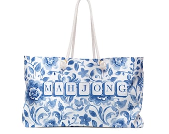 May include: A large tote bag with a white background and a blue floral pattern. The bag features the word "MAHJONG" in blue block letters. It has white rope handles with decorative knots.