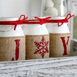 May include: Three white painted glass jars with burlap and red ribbon accents. The jars are decorated with the letters J, O, and Y, and a snowflake design.