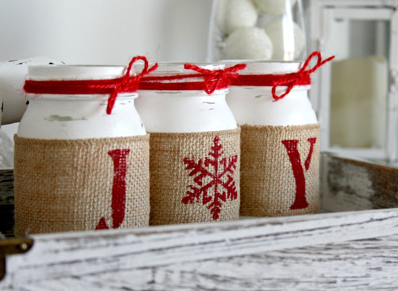 May include: Three white painted glass jars with burlap and red ribbon accents. The jars are decorated with the letters J, O, and Y, and a snowflake design.