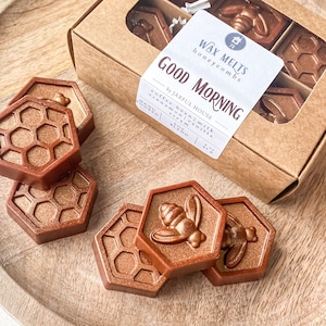 May include: A box of wax melts with a honeycomb design and the text "WAX MELTS honeycomb s GOOD MORNING by JARFUL HOUSE coffee bean | milk cinnamon | vanilla cream SOY BLEND". The wax melts are shaped like honeycombs and have a bee design.