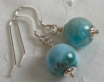 May include: A pair of silver dangle earrings with light blue round gemstone beads. The beads have a marbled pattern.