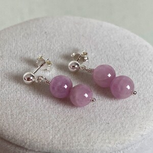 May include: A pair of silver earrings with two light purple round beads on each earring.