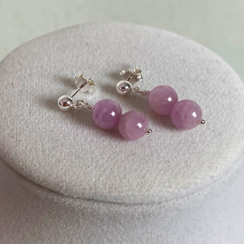 May include: A pair of silver earrings with two light purple round beads on each earring.