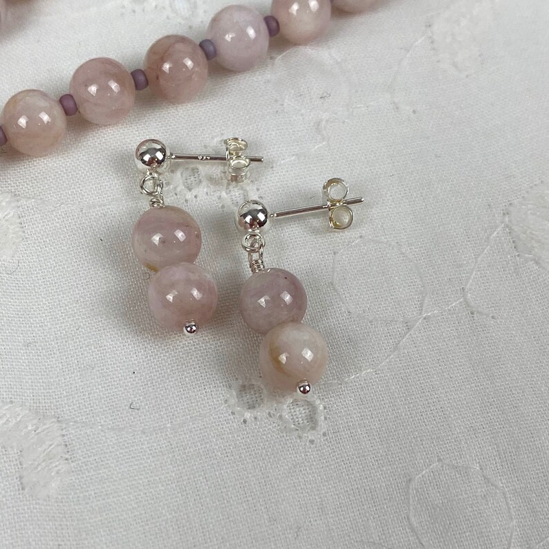 May include: A pair of silver earrings with two pale pink round gemstone beads on each earring.