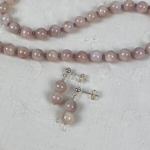 May include: A set of pink gemstone earrings and a matching necklace. The earrings are silver with a post back and feature two pink gemstone beads. The necklace is made of pink gemstone beads and silver.