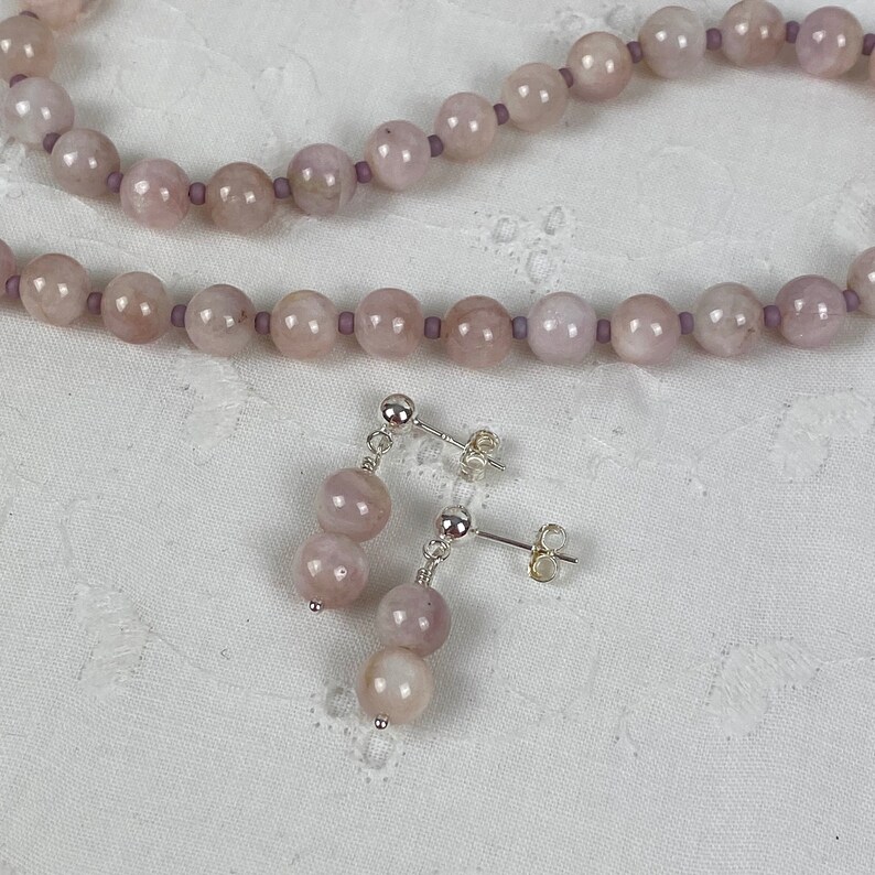 May include: A set of pink gemstone earrings and a matching necklace. The earrings are silver with a post back and feature two pink gemstone beads. The necklace is made of pink gemstone beads and silver.