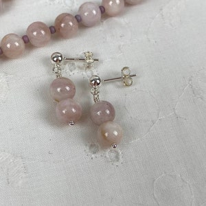 May include: A pair of silver earrings with two pale pink round gemstone beads on each earring.