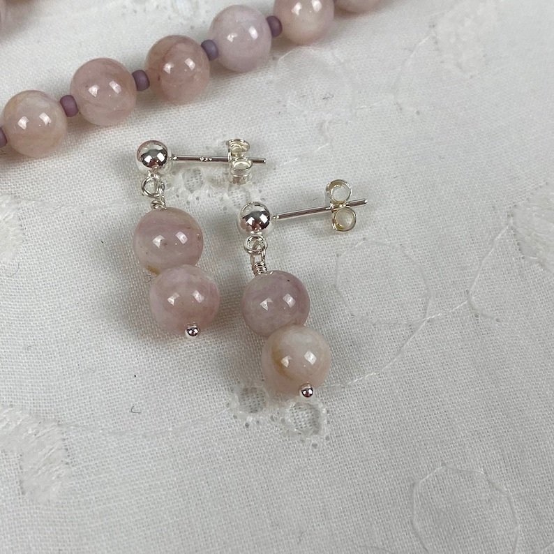 May include: A pair of silver earrings with two pale pink round gemstone beads on each earring.