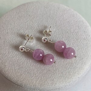 May include: A pair of silver dangle earrings with two lavender colored round beads on each earring.