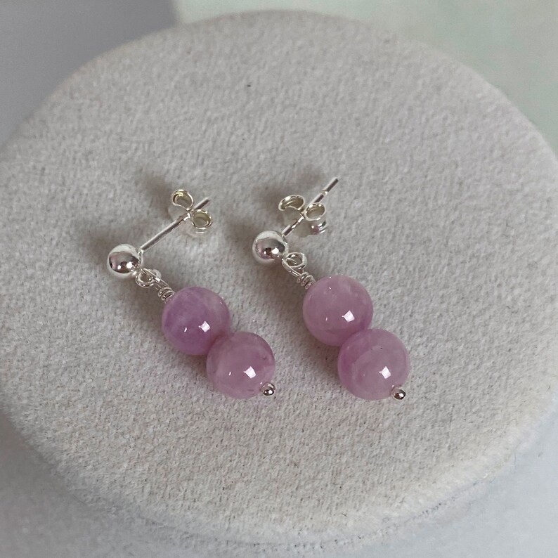May include: A pair of silver earrings with two lavender-colored round beads on each earring.