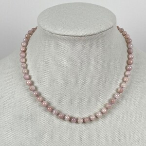 May include: A light pink gemstone necklace with round beads. The necklace is on a white mannequin.