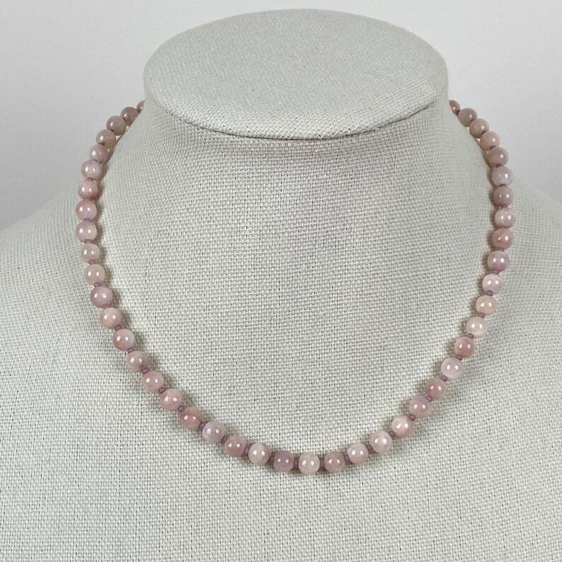 May include: A light pink gemstone necklace with round beads. The necklace is on a white mannequin.
