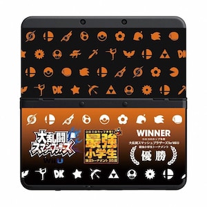 Puede incluir: Consola Nintendo 3DS negra con un diseño naranja y negro con varios iconos. La mitad inferior de la consola tiene texto japonés y la palabra "WINNER" en blanco. La consola está abierta.
