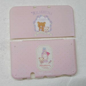 May include: Pink Nintendo 3DS case with Rilakkuma characters. The top cover features a floral design with a bear and a bunny. The bottom cover has a perfume bottle and a bear. Both covers have a polka dot pattern.
