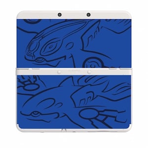 May include: A white Nintendo 3DS console with a blue skin featuring stylized illustrations of two creatures. The skin covers the top and bottom of the console. The text "AC ADAPTER" is visible on the bottom.