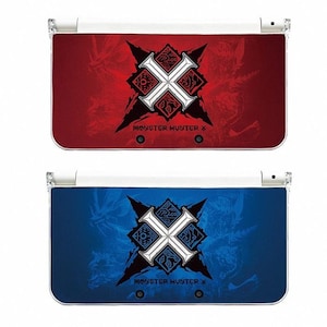 Può includere: Due console Nintendo 3DS, una rossa e una blu, ciascuna con un emblema centrale bianco e nero e la scritta "MONSTER HUNTER X". Le console hanno una finitura lucida e una parte superiore in plastica trasparente.