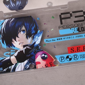 May include: Clear plastic case featuring a character illustration with blue hair and eyes. The case has the text "P3 PERSONA3 RELOAD" and "S.E.E.S" in black and red. The case also has Japanese text and the "Persona 3 Portable" logo.