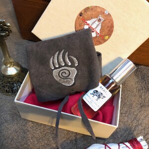 May include: A white gift box containing a dark gray suede pouch with a silver bear paw print, a small glass spray bottle of essential oil perfume labeled BEAT with a bear graphic, and a round sticker featuring a bear illustration.