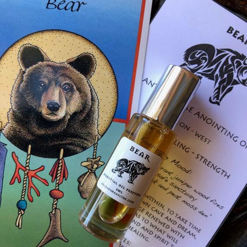 May include: A clear glass roller bottle of Bear essential oil perfume with a silver cap and a white label featuring a black bear illustration and the text Bear Essential Oil Perfume 5ml. The bottle rests on a card with a bear graphic.