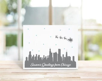 May include: A white card with a gray silhouette of the Chicago skyline and Santa Claus flying over the city with reindeer. The card reads "Season's Greetings from Chicago".