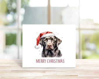May include: A chocolate Labrador Retriever wearing a red Santa hat with white trim. The dog is looking directly at the viewer. The background is white with a few snowflakes. The text "Merry Christmas" is printed in red below the dog.