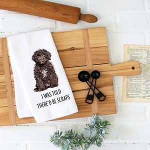 May include: White kitchen towel with a brown dog sitting on it. The dog is looking at the camera. The text "I was told there'd be scraps" is printed below the dog.