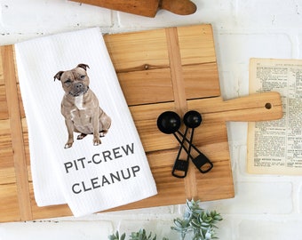 Op de afbeelding: Een witte keukendoek met een bruine en witte pit bull terrier hond erop gedrukt. De tekst "PIT-CREW CLEANUP" is in grijs onder de hond gedrukt.