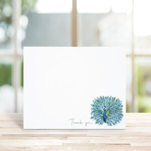 May include: A white thank you card with a blue and green peacock illustration. The peacock is facing right with its tail feathers spread out. The text "Thank you" is written in cursive at the bottom of the card.