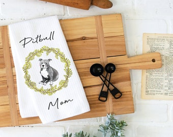 Op de afbeelding: Een witte keukendoek met een groene krans en een aquarel-illustratie van een grijze Pitbull-hond. De tekst "Pitbull Mom" is op de doek gedrukt.