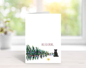 May include: A white greeting card featuring a watercolor illustration of a horizontal green Christmas tree decorated with colorful lights, a small yellow star, and a black dog sitting next to it, with the red text ALL IS CALM...