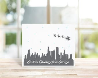 May include: A white card with a gray silhouette of the Chicago skyline and Santa Claus flying over the city with reindeer. The card reads "Season's Greetings from Chicago".