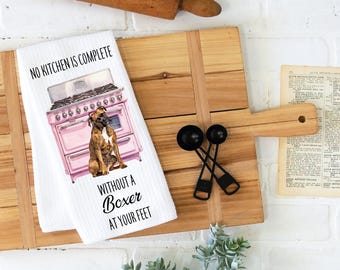 May include: White kitchen towel with a pink retro stove and a brown Boxer dog sitting in front of it. The text on the towel reads "No kitchen is complete without a Boxer at your feet."