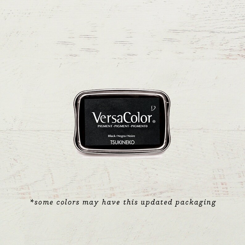 May include: A black ink pad with a silver metal casing. The ink pad is labeled "VersaColor" and "Black/Negra/Noire" with the brand name "TSUKINEKO".