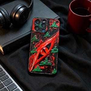 Könnte beinhalten: Eine rechteckige Smartphone-Hülle mit einem strukturierten, abstrakten Design und einem markanten zentralen roten Augenmotiv. Die Oberfläche zeigt wirbelnde schwarze und rote farbähnliche Texturen, akzentuiert durch kleine, erhabene grüne baumförmige Verzierungen.