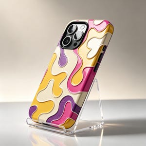 Puede incluir: Una funda para smartphone con un patrón ondulado en relieve de varios colores en tonos crema, amarillo, magenta y morado. La funda tiene un recorte negro para el módulo de cámara con tres lentes circulares y un flash, apoyada en un soporte acrílico.