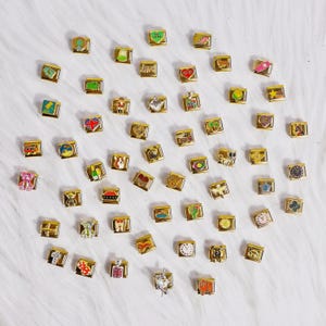 Puede incluir: Una colección de charms dorados con varios diseños, incluyendo corazones, animales y símbolos. Los charms están dispuestos sobre una superficie blanca y peluda.