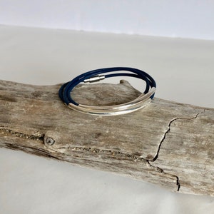 May include: A navy blue leather bracelet with a silver metal band. The bracelet is wrapped around a piece of driftwood.
