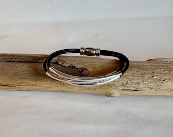 May include: A black leather bracelet with a silver bar accent. The bracelet has a magnetic clasp.