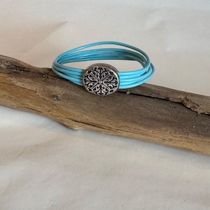 Manschettenarmband aus feinem hellblauen italienischen Leder. Akzentuiert mit einem detaillierten Silberknopf und einem Silbermagnetverschluss. 7&quot; Länge.