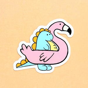 May include: A die-cut sticker featuring a light blue dinosaur with yellow dorsal plates standing inside a pink flamingo-shaped pool float. The flamingo has a long neck, a black and white beak, and a simple black eye, all outlined in bold black lines.