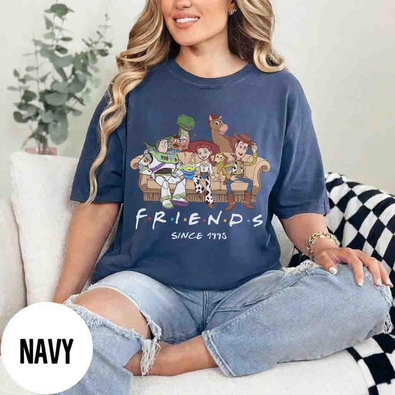 May include: A navy blue short-sleeve t-shirt featuring a graphic print of Toy Story characters sitting on a couch. The text reads "F R I E N D S" above "SINCE 1995". The characters include Buzz Lightyear, Rex, Jessie, Slinky Dog, Bullseye, and Woody.
