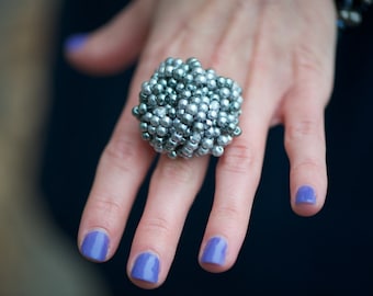 May include: A large silver ring with a cluster of small, round beads. The ring is worn on a hand with purple nail polish.